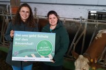 2 Personen halten ein Plakat in einem Stall